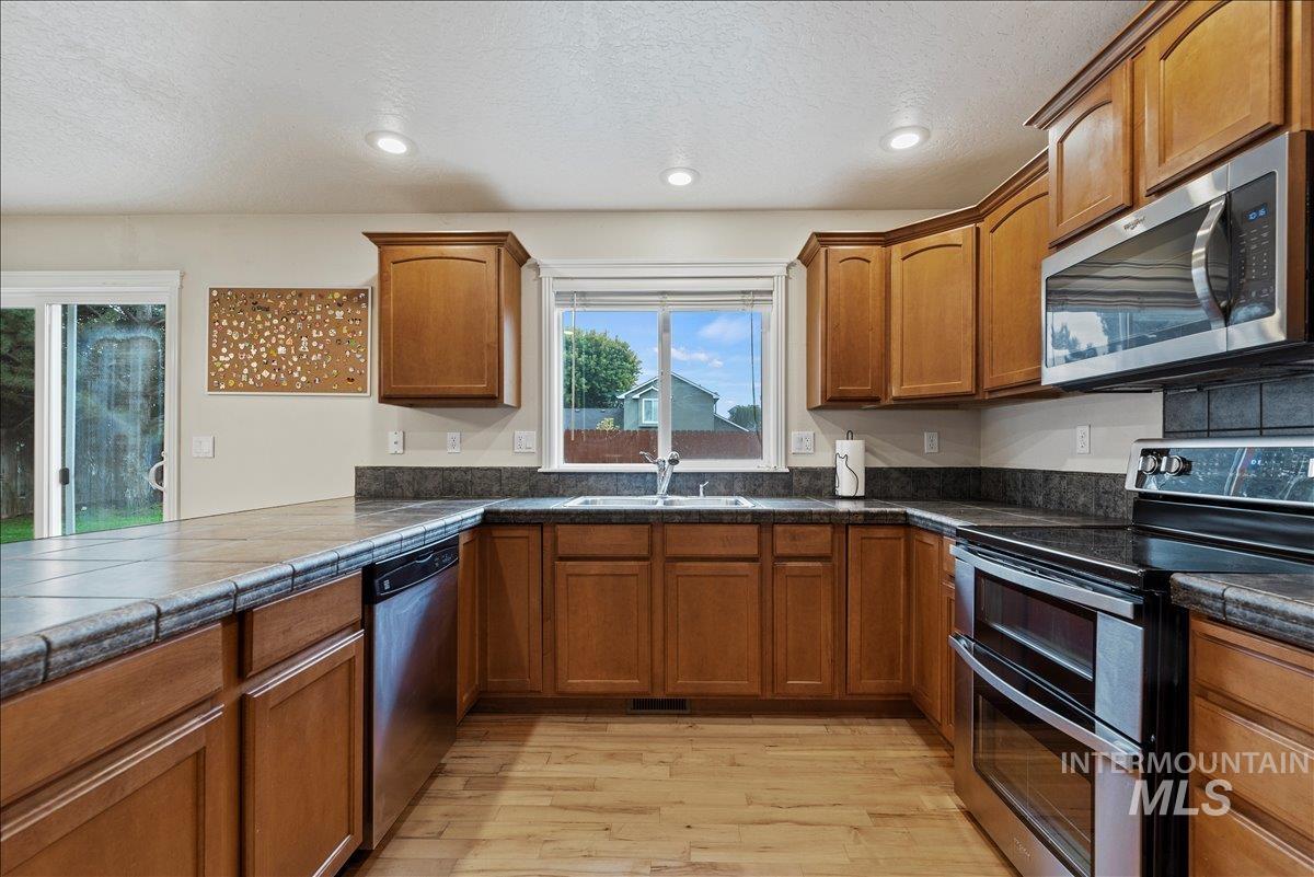 Kitchen with appliances with stainless steel finishes, brown cabinetry, light wood finished floors, a textured ceiling, and recessed lighting