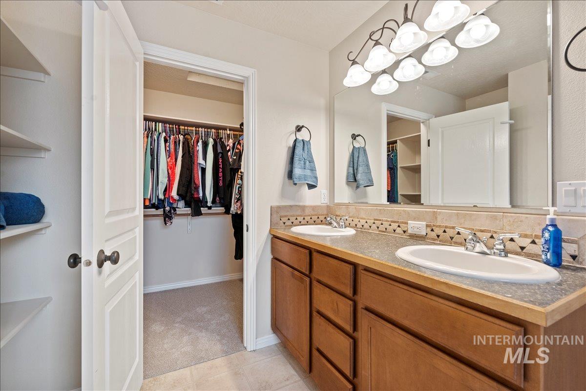 Bathroom featuring a spacious closet, double vanity, decorative backsplash, and a chandelier