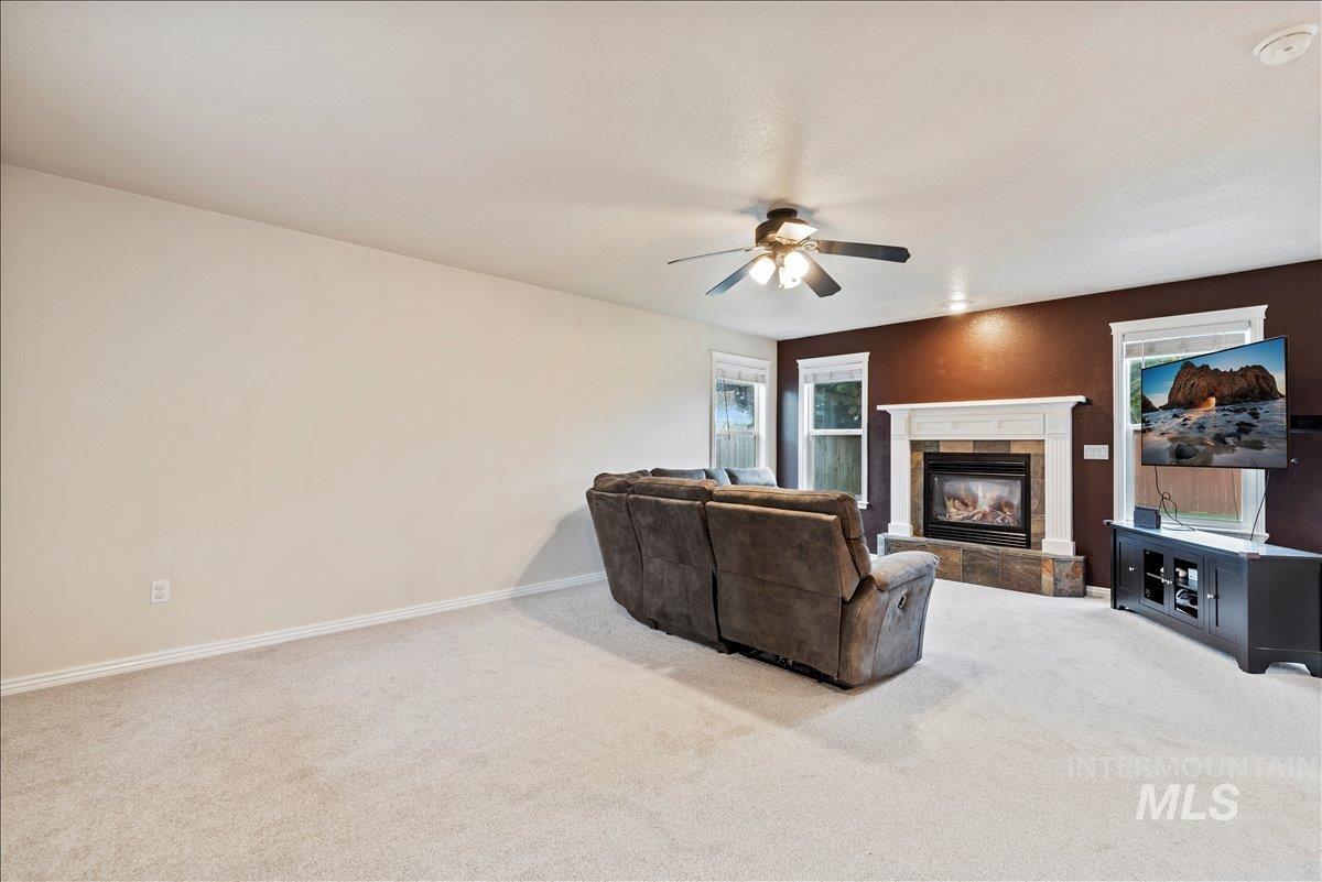 Carpeted living area featuring a tiled fireplace, a ceiling fan, and a textured ceiling