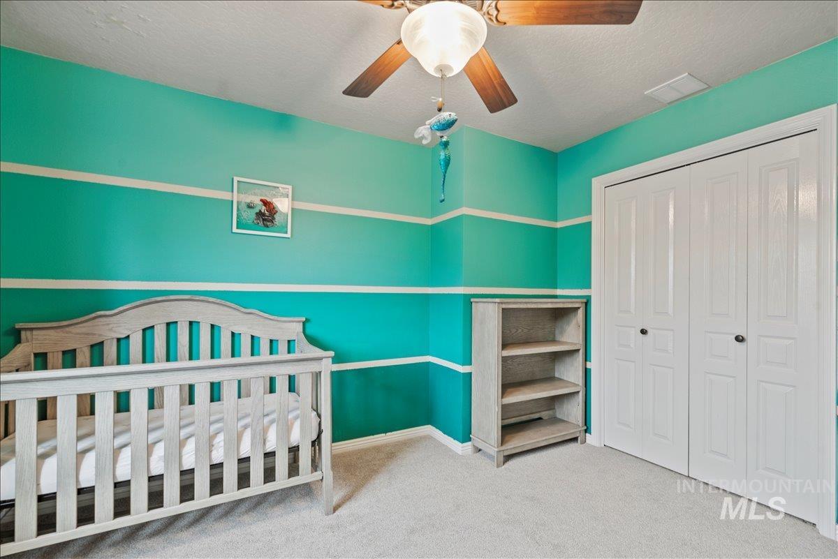Bedroom with light colored carpet, a textured ceiling, a closet, a ceiling fan, and a nursery area