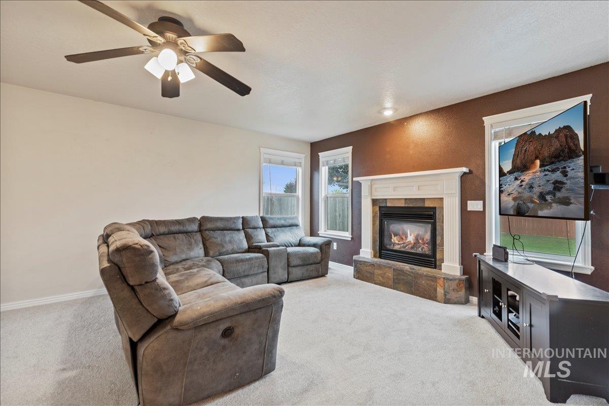 Living room with light colored carpet, a tiled fireplace, and a ceiling fan