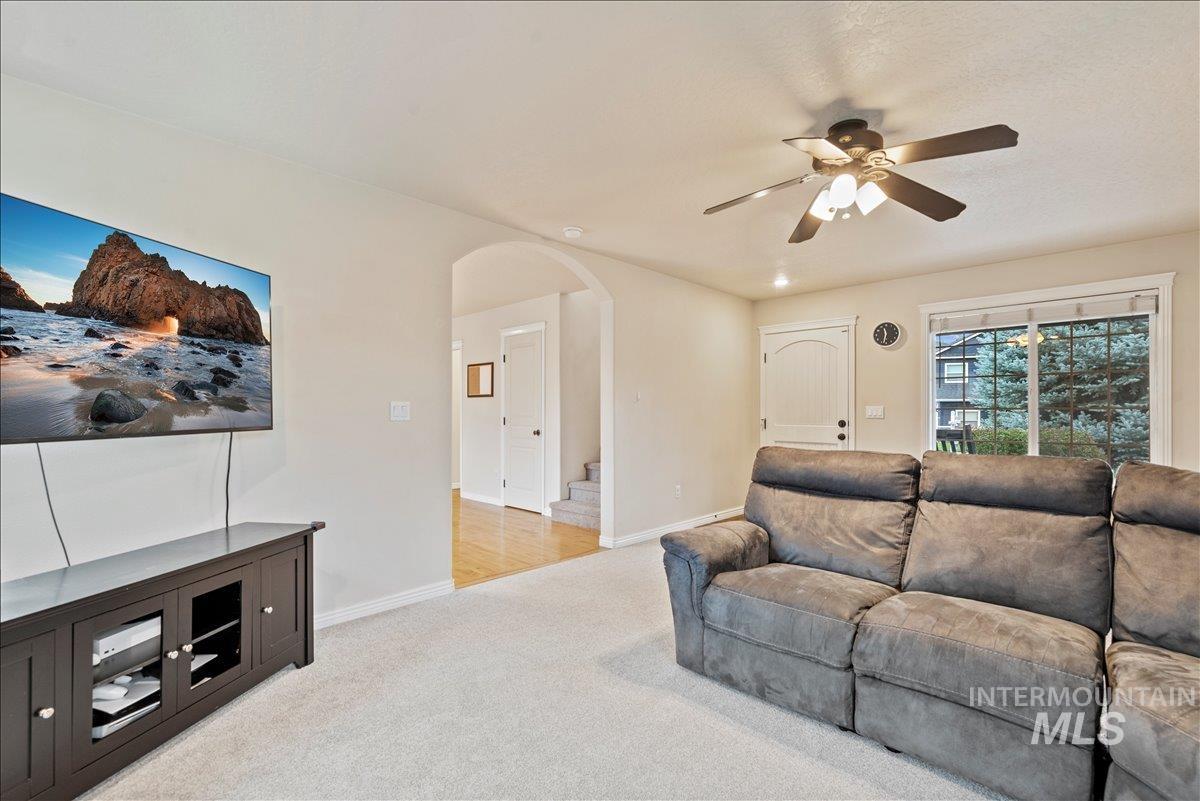Living area featuring light colored carpet, arched walkways, ceiling fan, and stairs