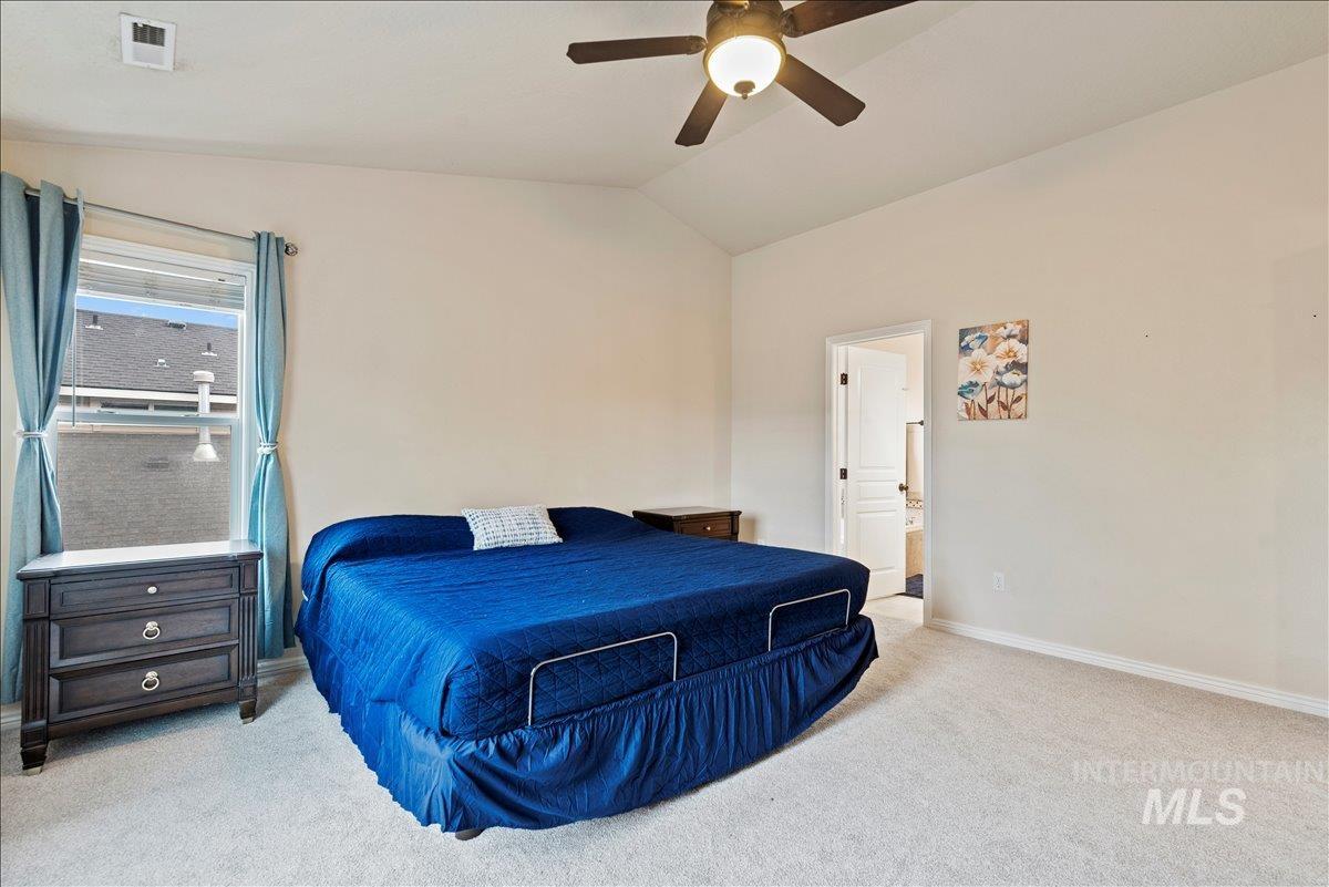 Bedroom with light colored carpet, lofted ceiling, ceiling fan, and connected bathroom