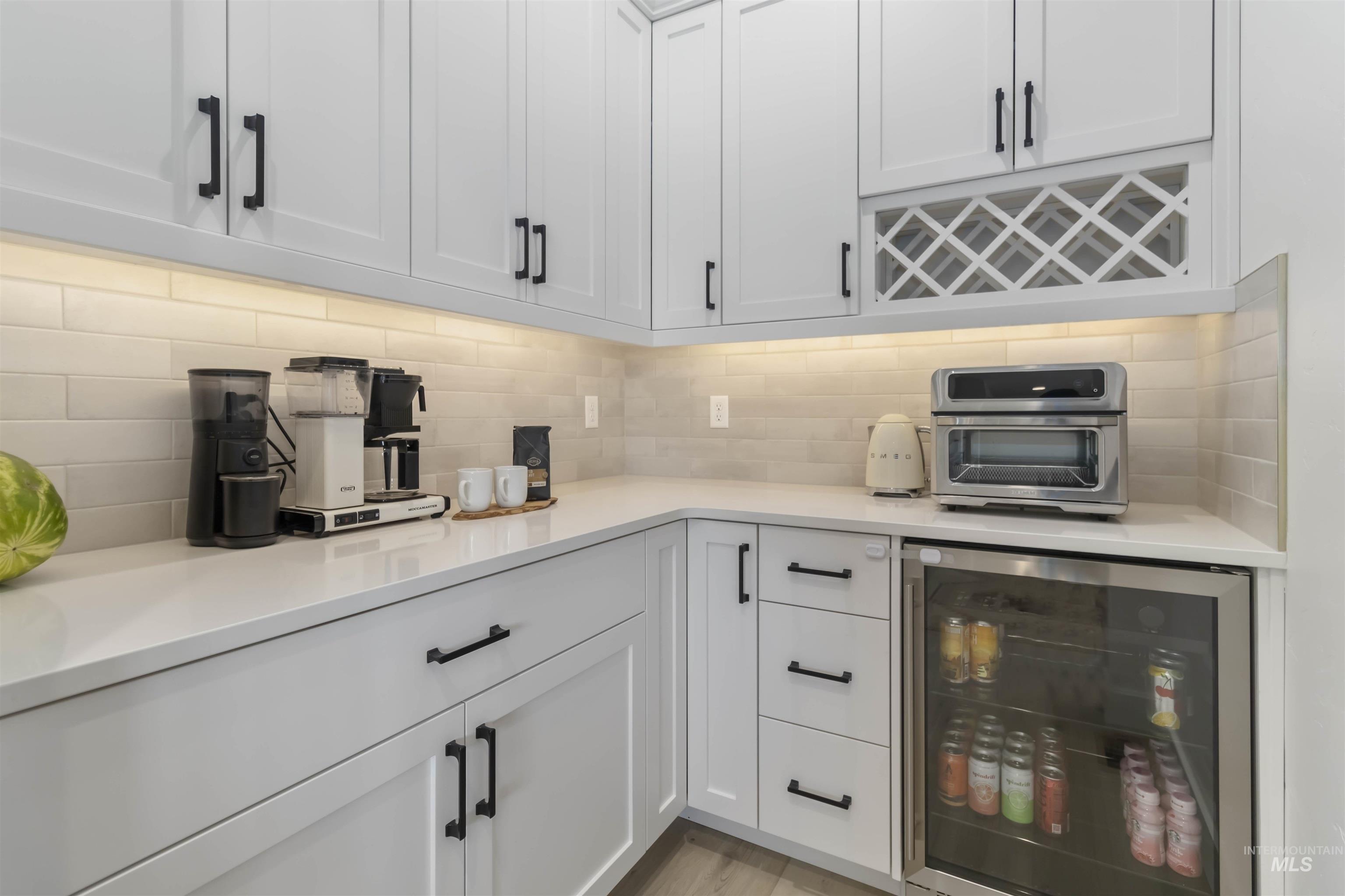 Kitchen with wine cooler, white cabinetry, backsplash, and light stone counters