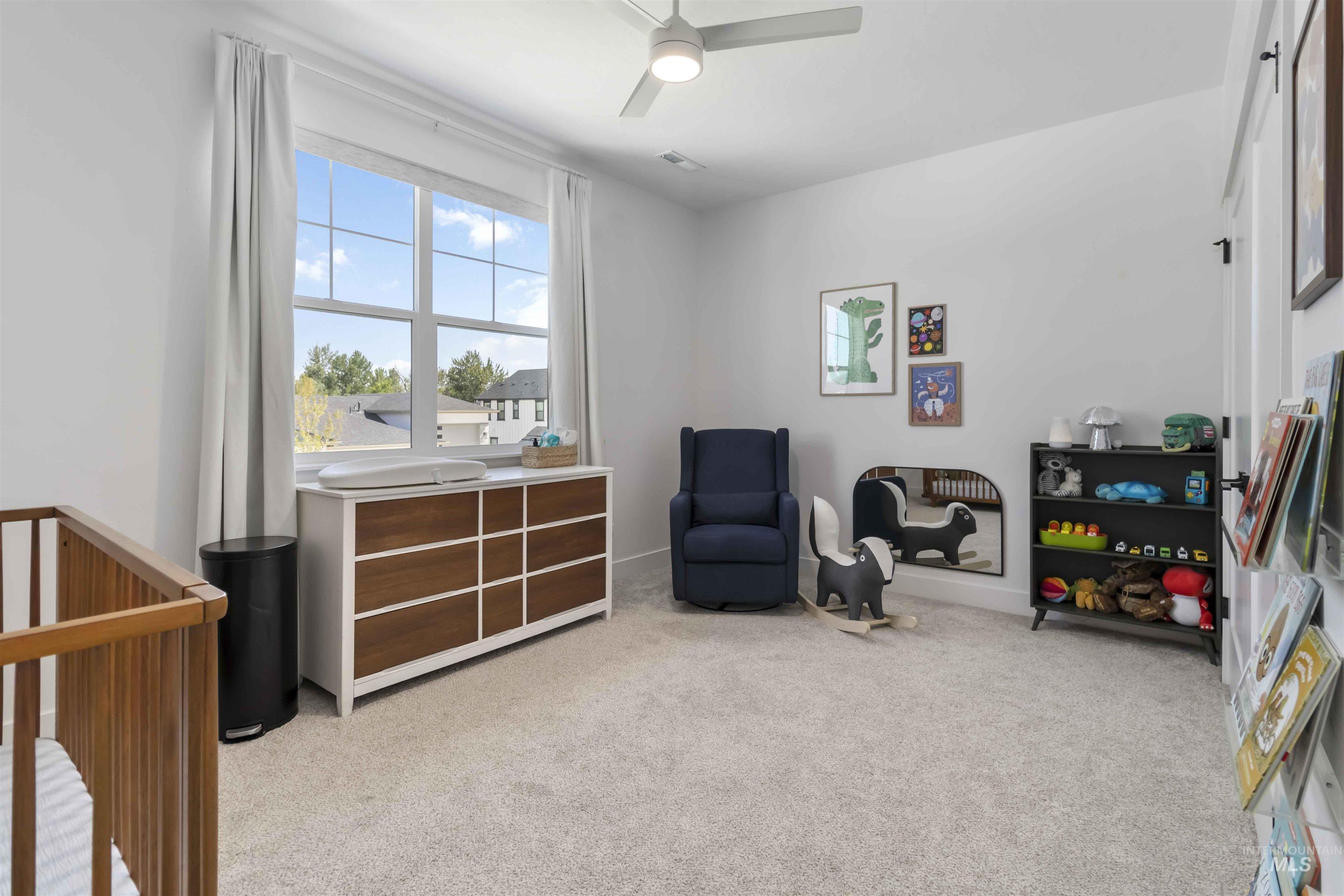 Bedroom featuring a crib, light carpet, and a ceiling fan
