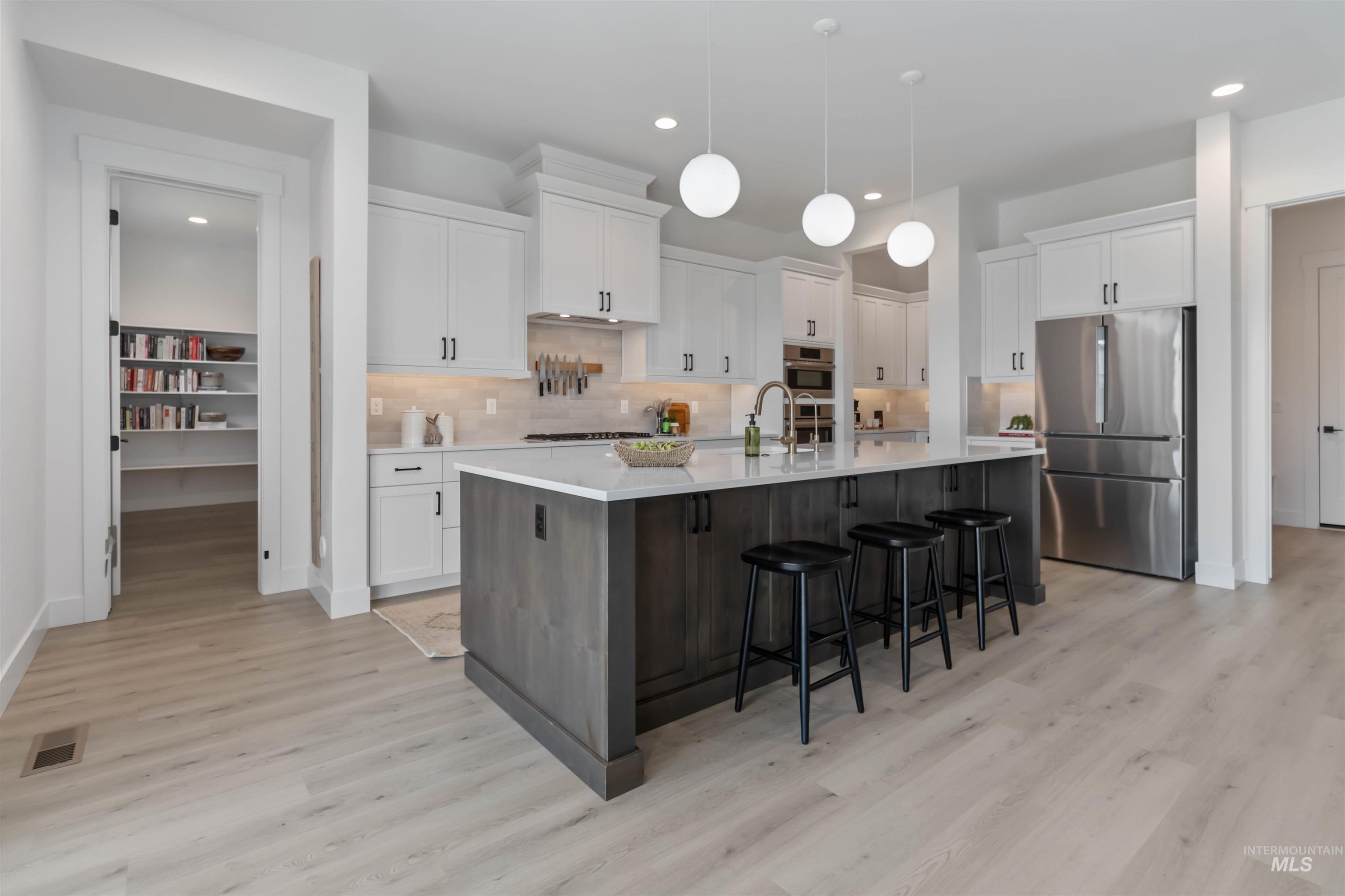 Two tone kitchen with dual tone cabinets, stainless steel appliances, a large island with sink, a breakfast bar area, and light wood-style floors