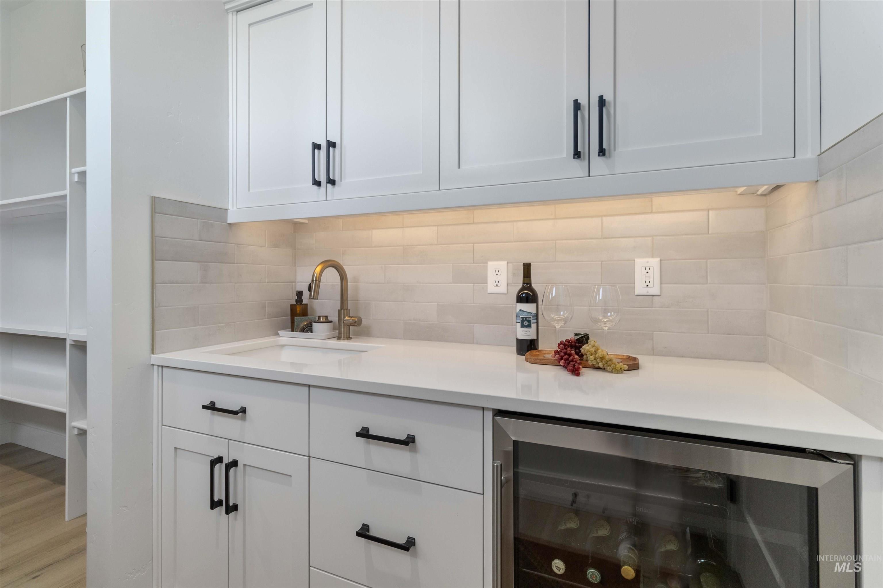 Bar area featuring beverage cooler, white cabinets, decorative backsplash, and light stone counters