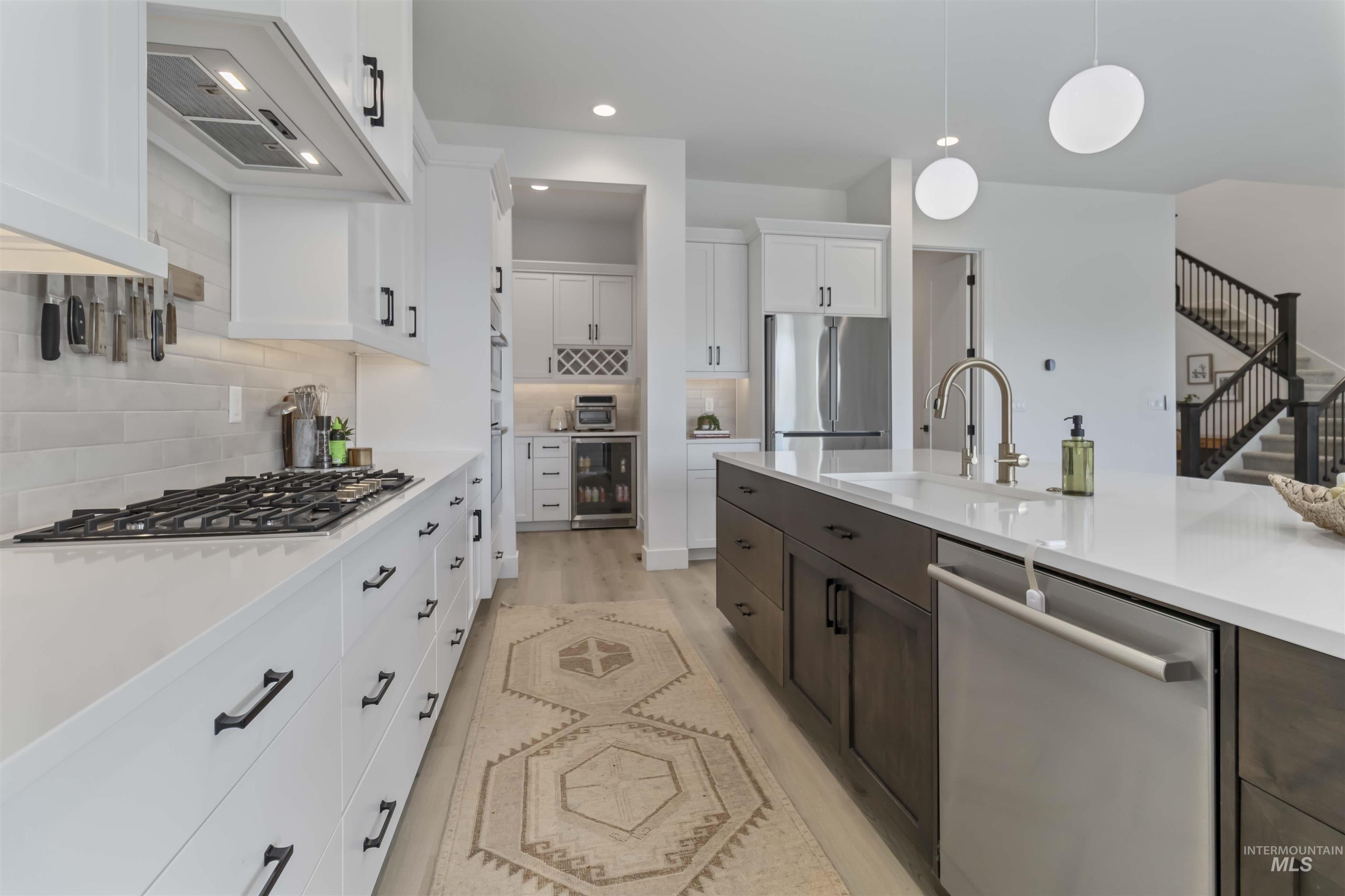 Kitchen with stainless steel appliances, extractor fan, beverage cooler, two tone color scheme, and hanging light fixtures
