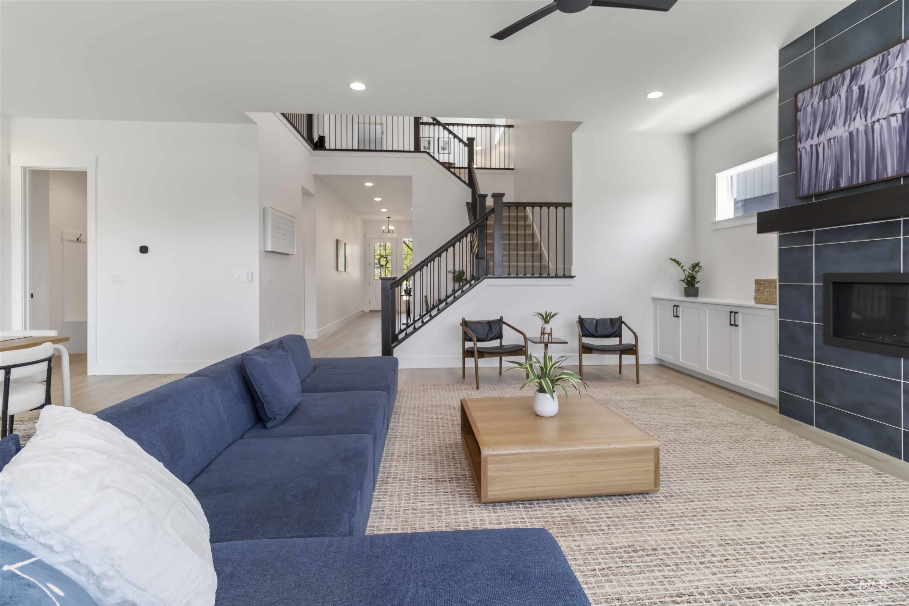 Living room featuring a fireplace, a ceiling fan, a high ceiling, recessed lighting, and light wood finished floors