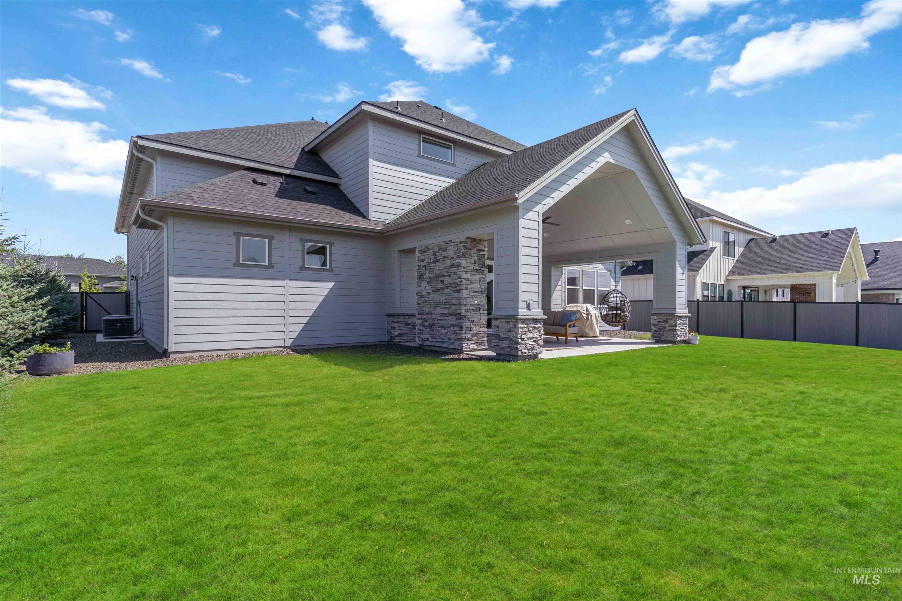 Back of property featuring a fenced backyard, a patio area, roof with shingles, and stone siding