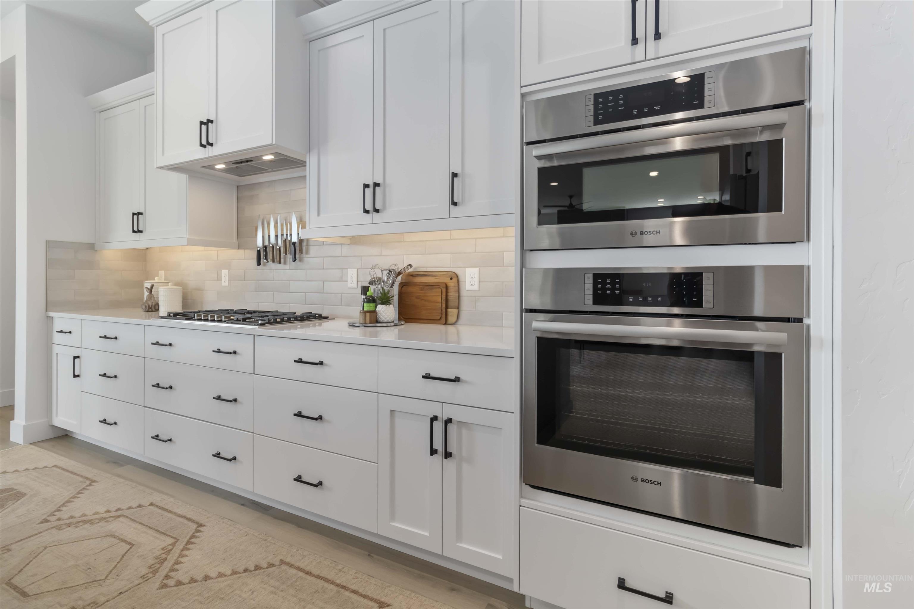 Kitchen featuring stainless steel appliances, white cabinets, light stone counters, and decorative backsplash