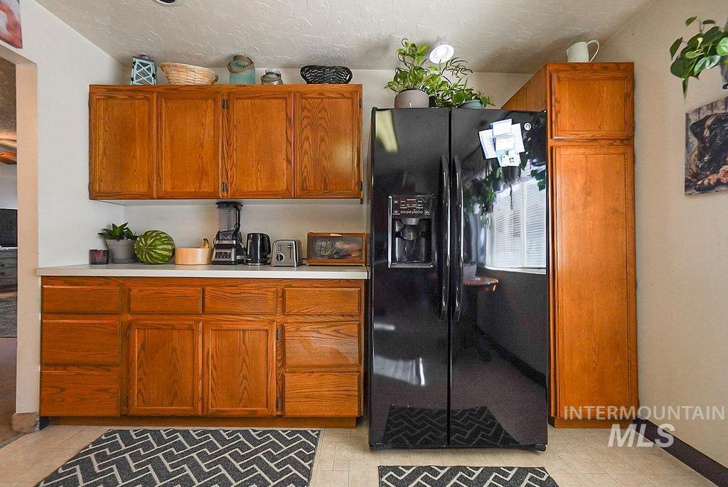 Kitchen with black fridge with ice dispenser, light countertops, brown cabinetry, a textured ceiling, and light tile patterned flooring