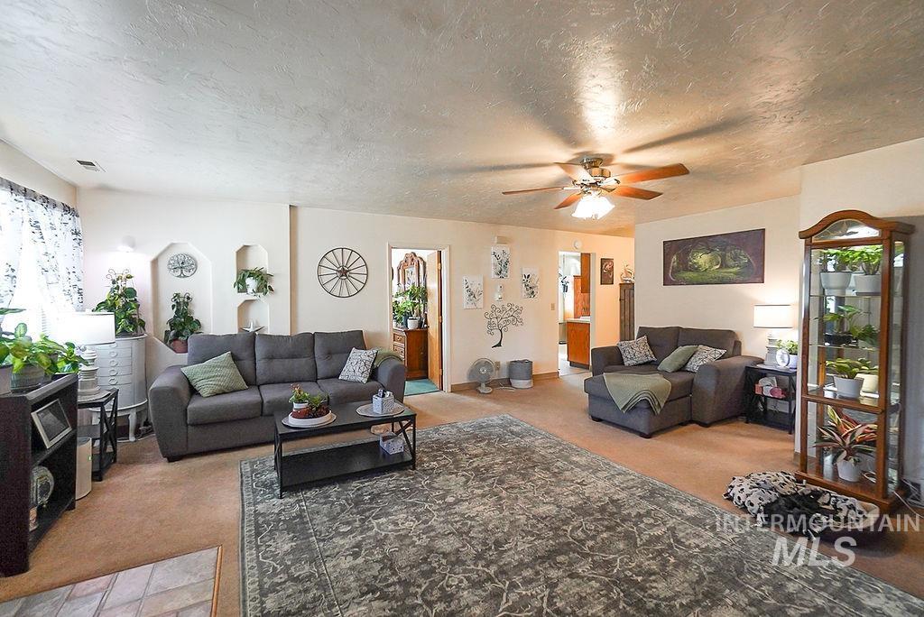 Living area featuring a textured ceiling, ceiling fan, light carpet, and healthy amount of natural light