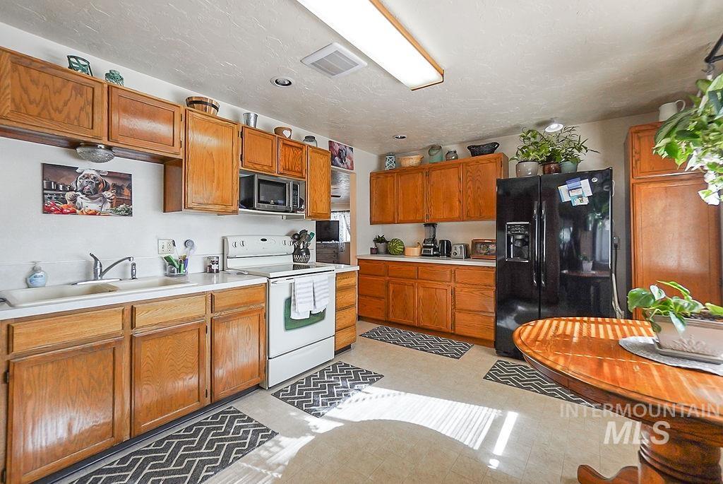 Kitchen featuring light countertops, black appliances, brown cabinets, and a textured ceiling