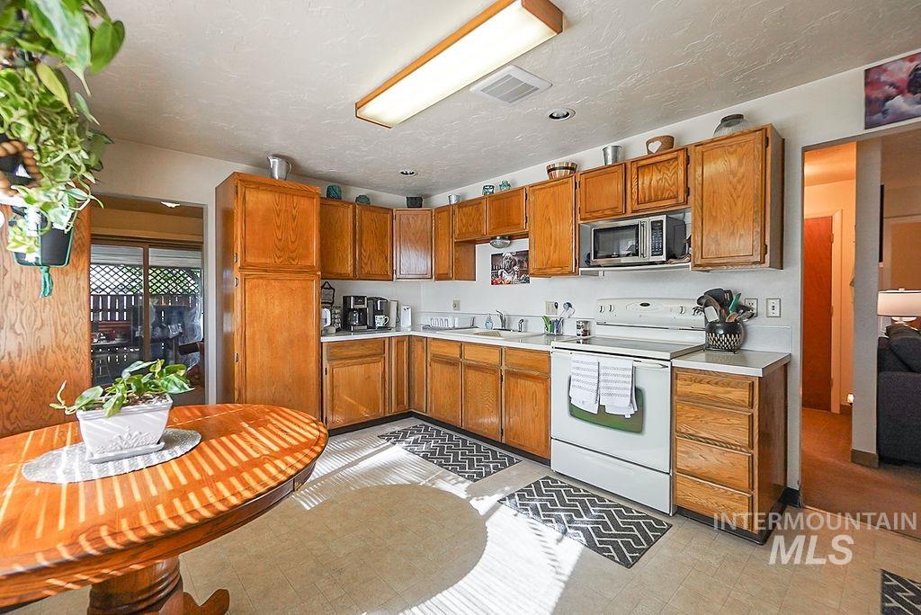 Kitchen with white range with electric cooktop, light countertops, brown cabinetry, stainless steel microwave, and a textured ceiling