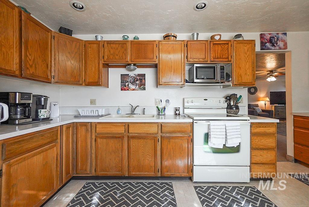Kitchen featuring white electric range oven, light countertops, brown cabinetry, stainless steel microwave, and a textured ceiling