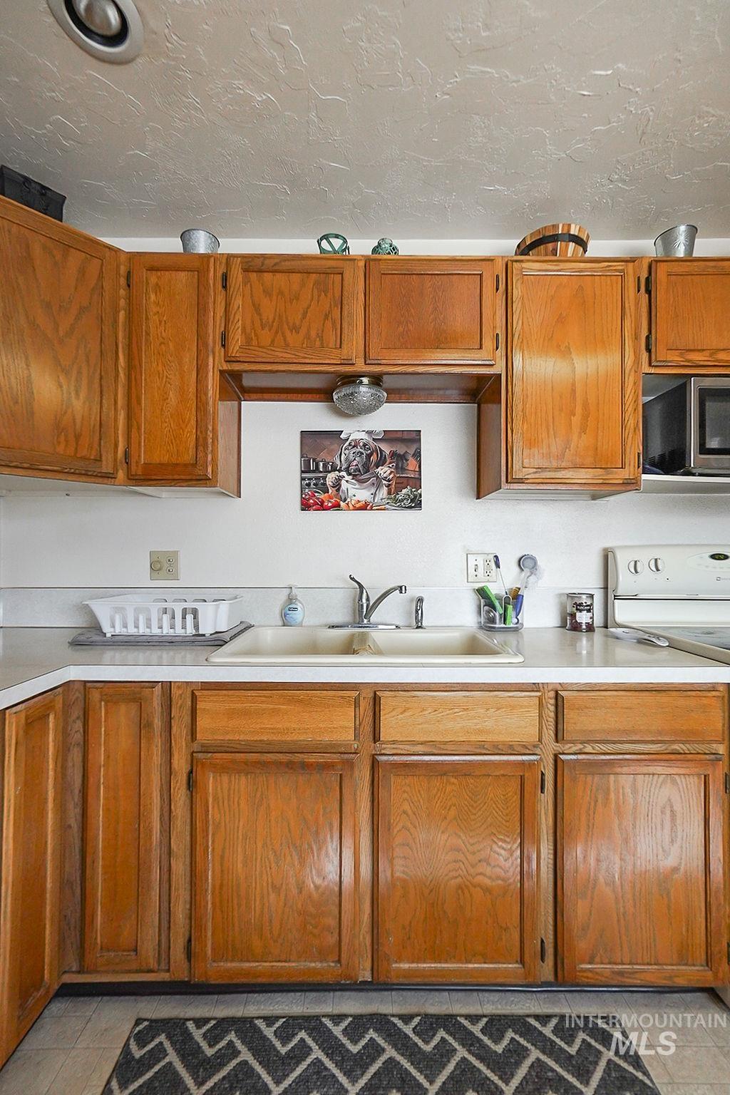 Kitchen featuring light tile patterned flooring, light countertops, brown cabinetry, a textured ceiling, and stainless steel microwave