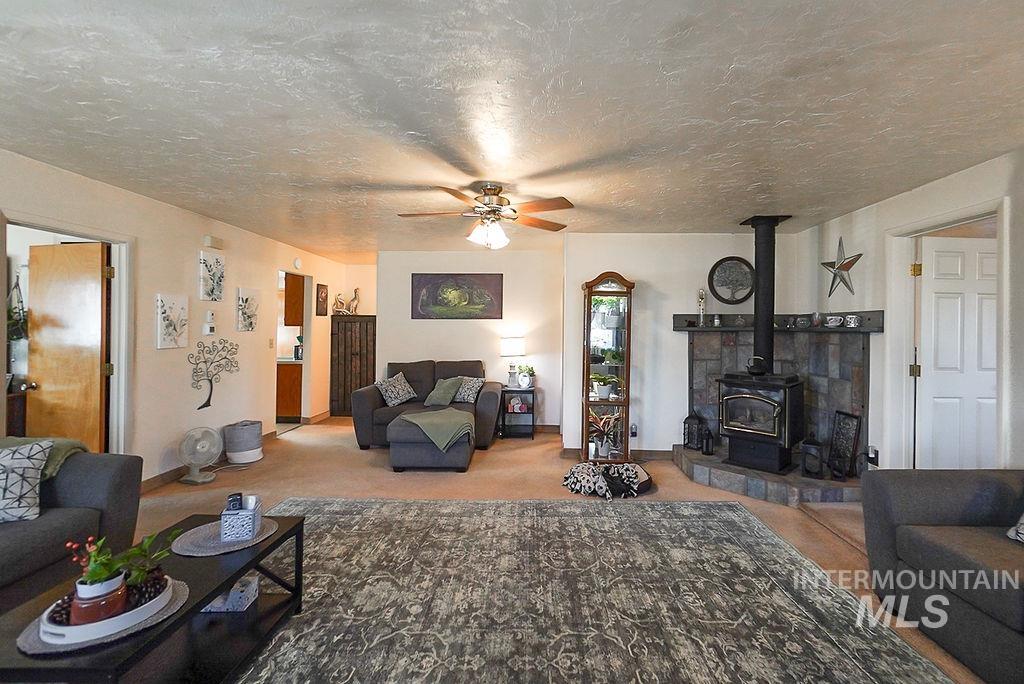 Living room featuring a wood stove, ceiling fan, a textured ceiling, and light colored carpet