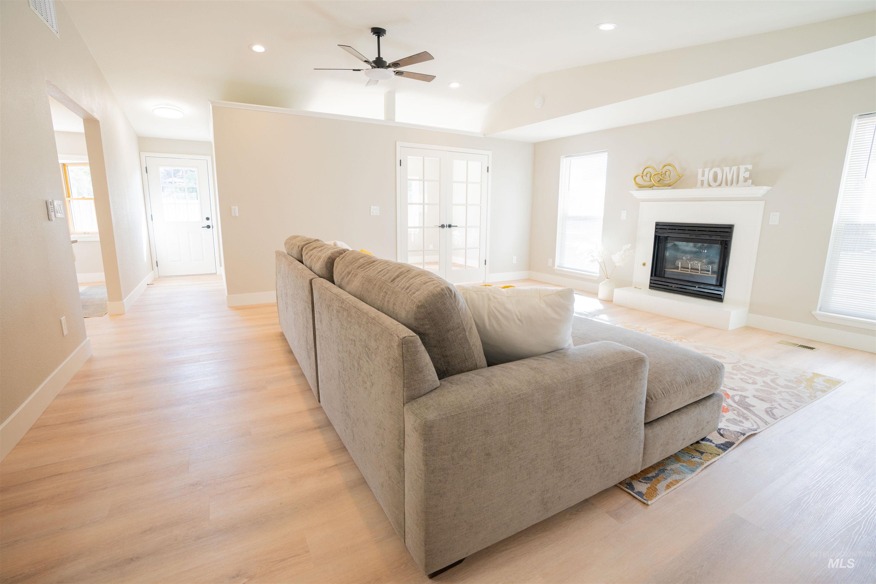 Living room with recessed lighting, a glass covered fireplace, light wood-style floors, a ceiling fan, and vaulted ceiling