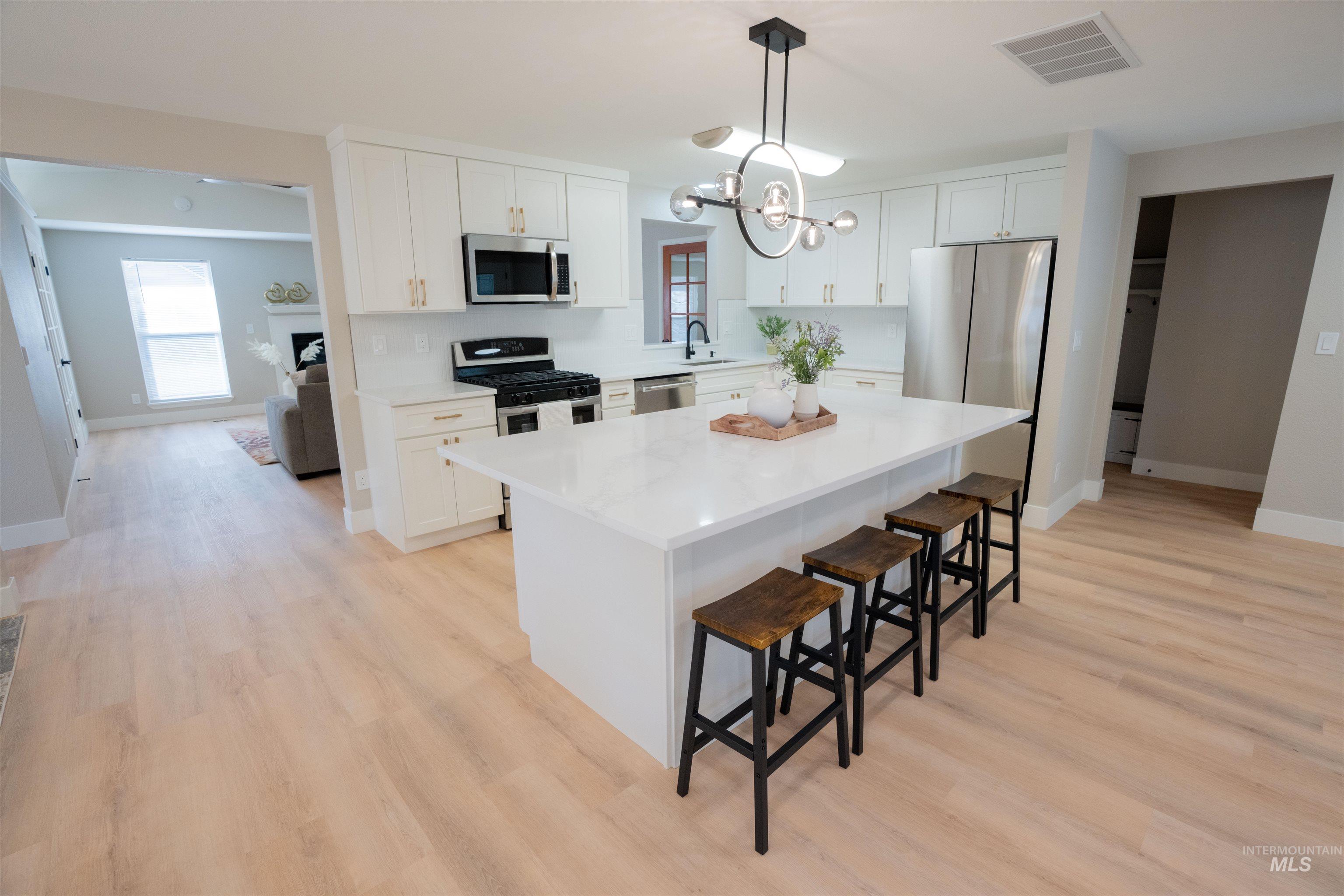 Kitchen with white cabinets, a kitchen island, appliances with stainless steel finishes, and pendant lighting