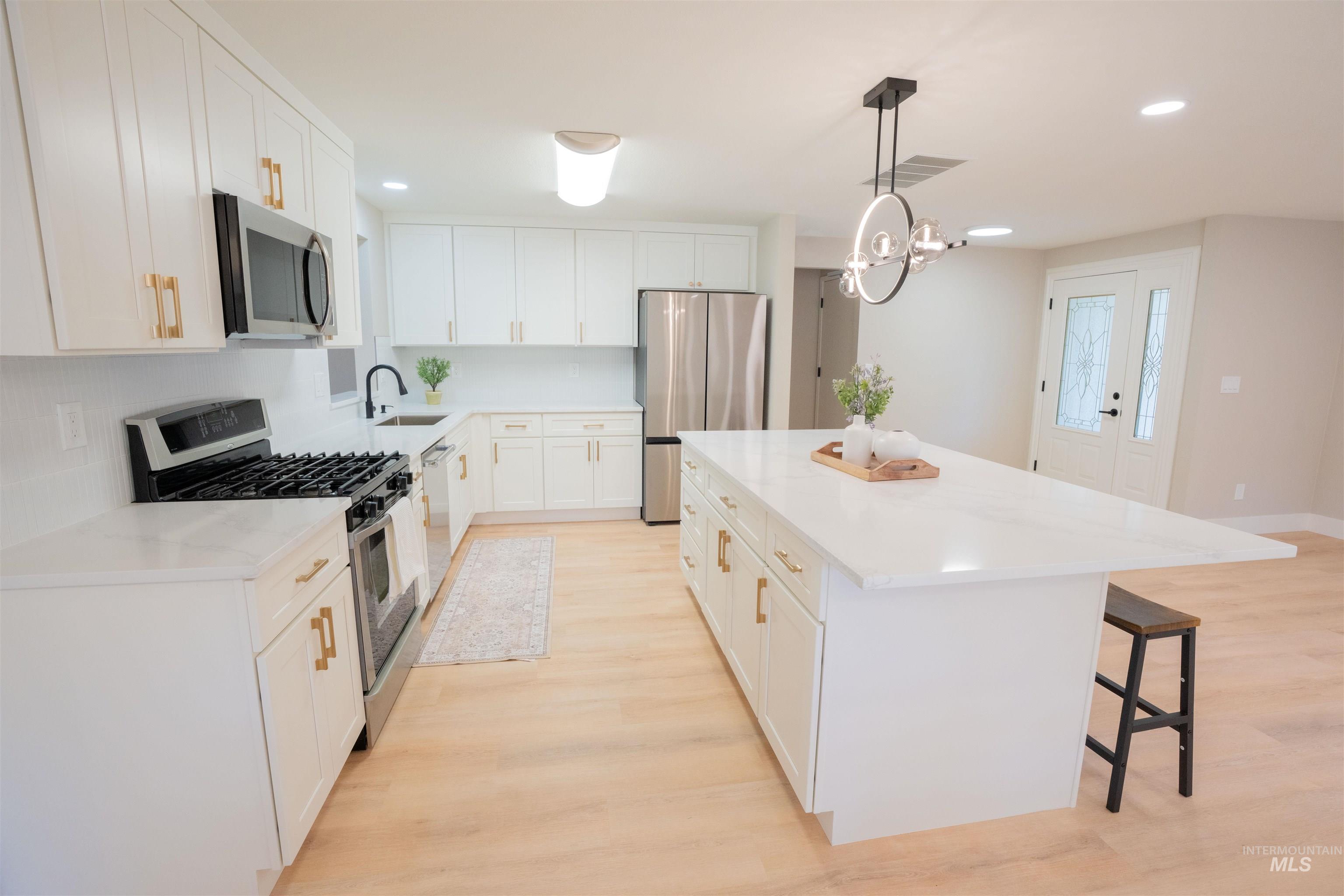 Kitchen featuring appliances with stainless steel finishes, a kitchen bar, white cabinetry, a center island, and light wood-type flooring