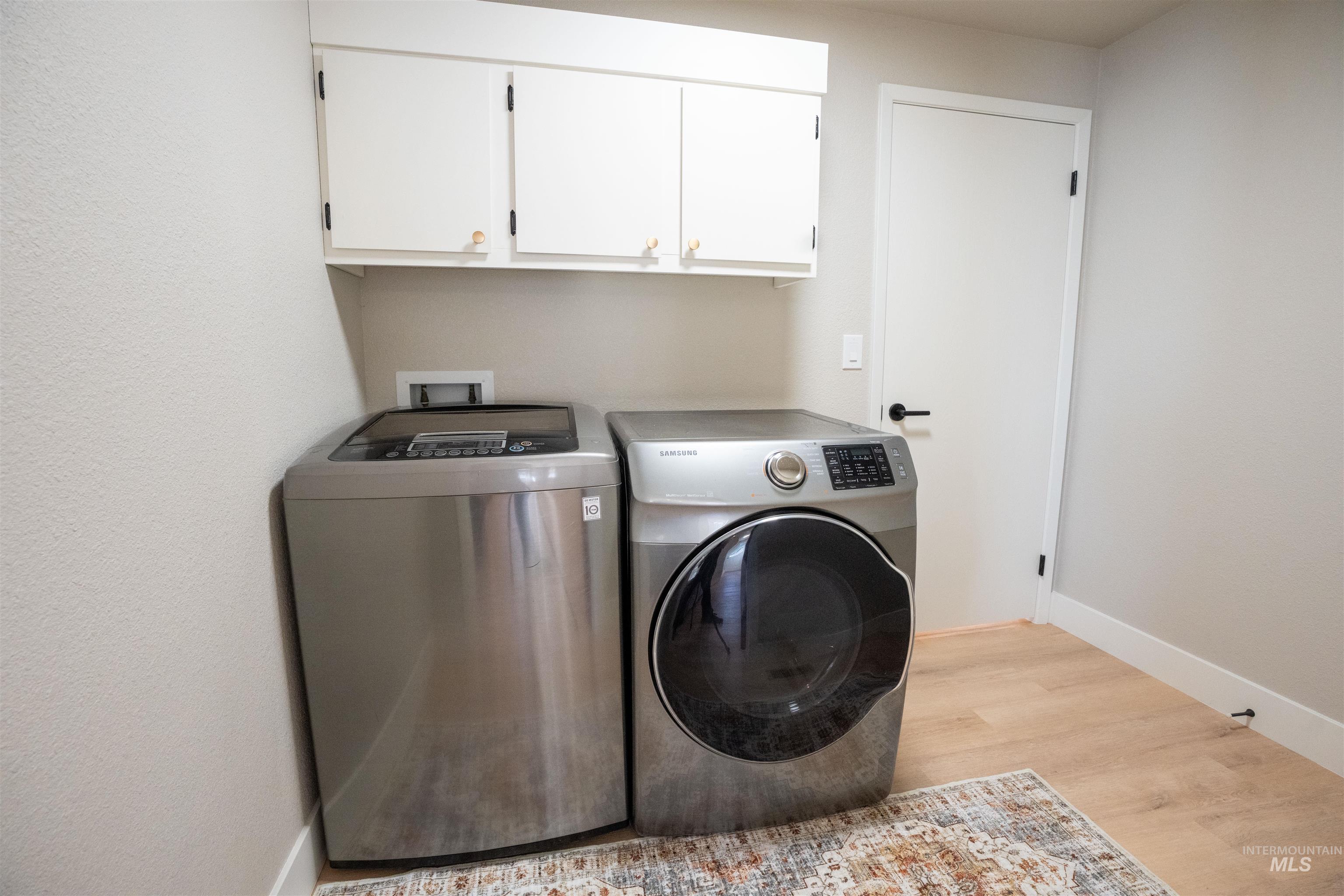 Laundry area with separate washer and dryer, light wood-style flooring, and cabinet space