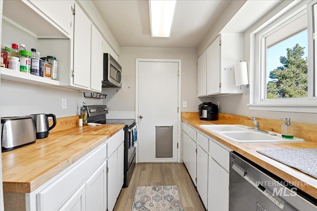 Galley kitchen featuring wood-finish countertops, white cabinetry, and stainless steel appliances including a built-in microwave and dishwasher