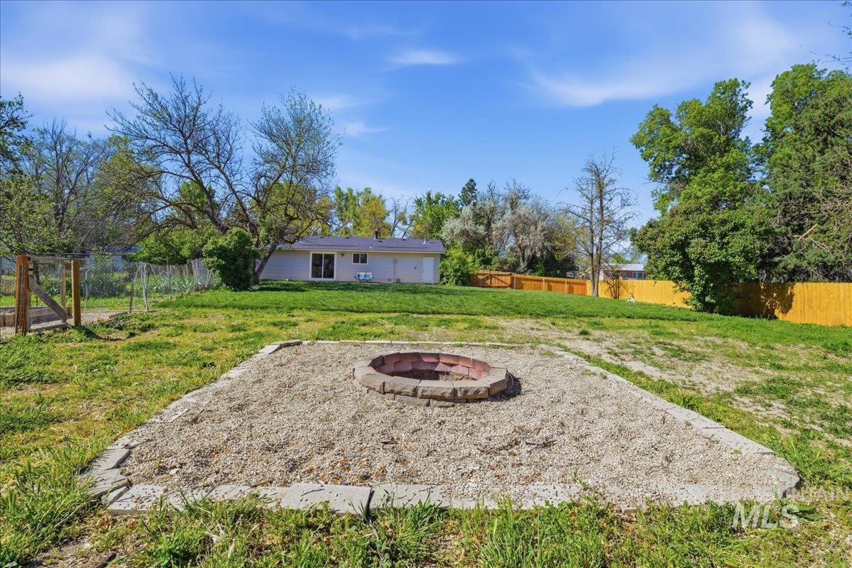Expansive backyard featuring a stone-edged fire pit area with gravel, a wooden privacy fence, and mature trees