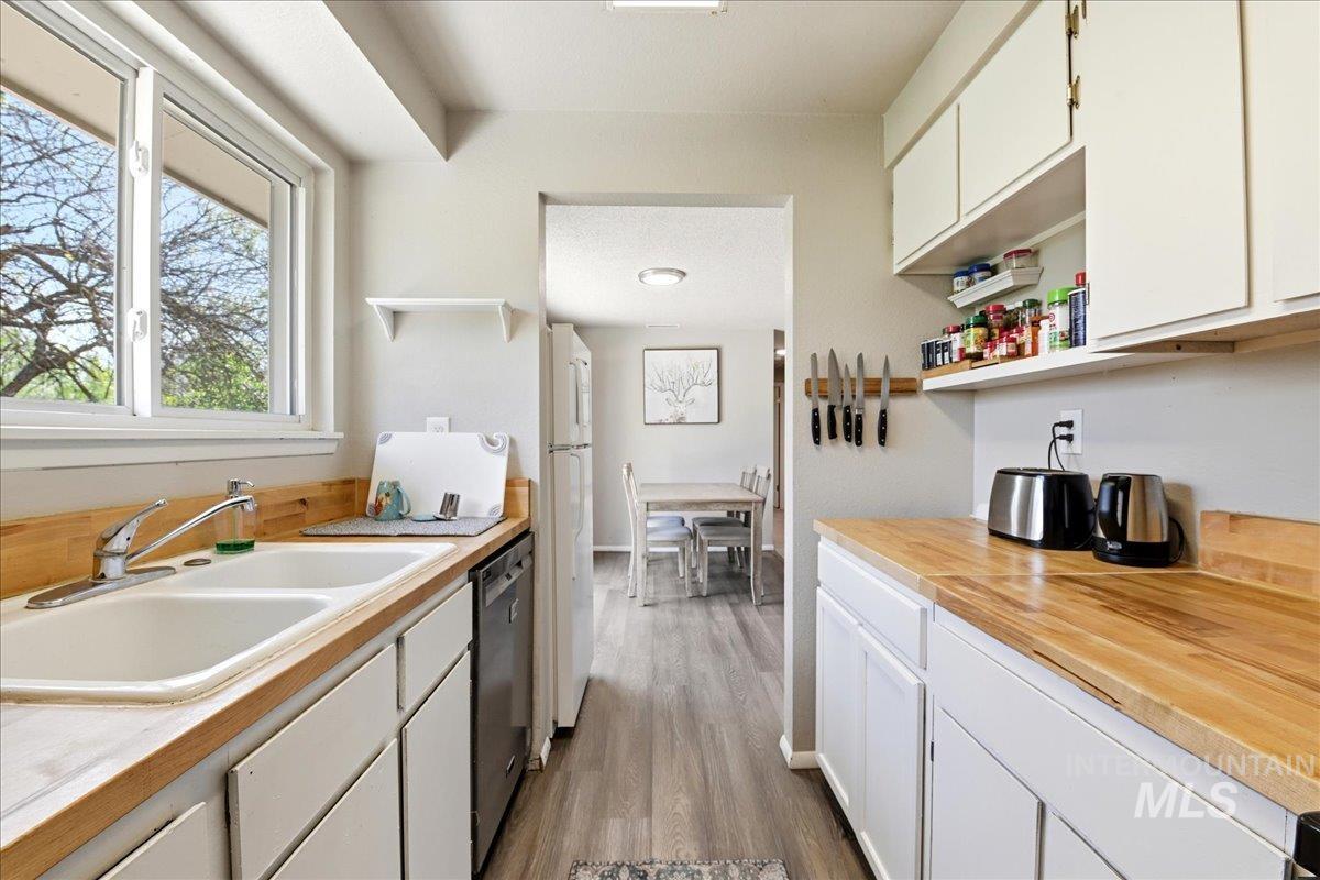 Kitchen featuring wood-finish countertops, white cabinetry, a double basin sink, and wood-finish flooring