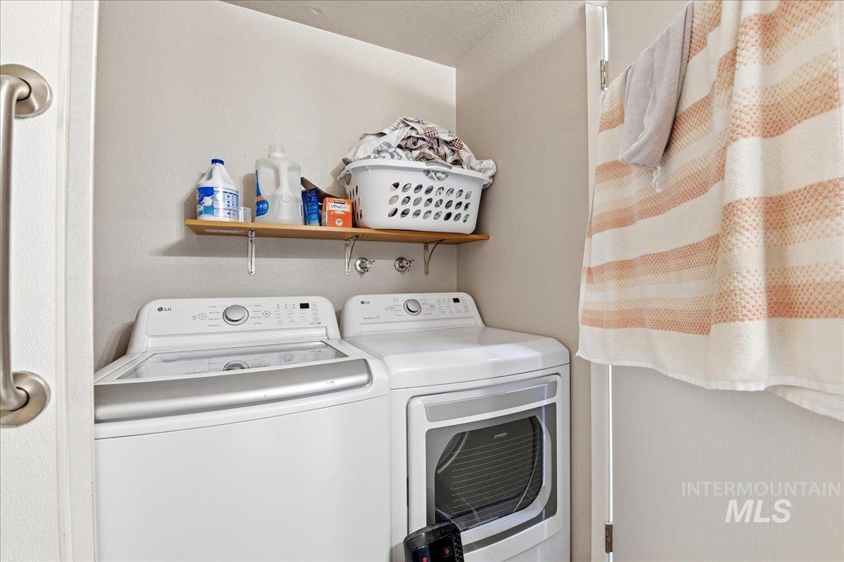 Dedicated laundry area featuring a washer and dryer, an overhead wooden shelf, and a wall-mounted grab bar