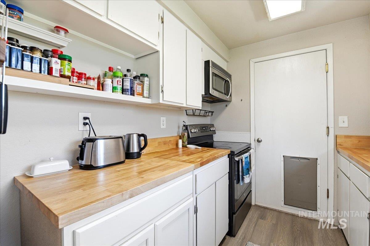 Kitchen featuring wood-finish countertops, white cabinetry, a built-in microwave, and a black electric range