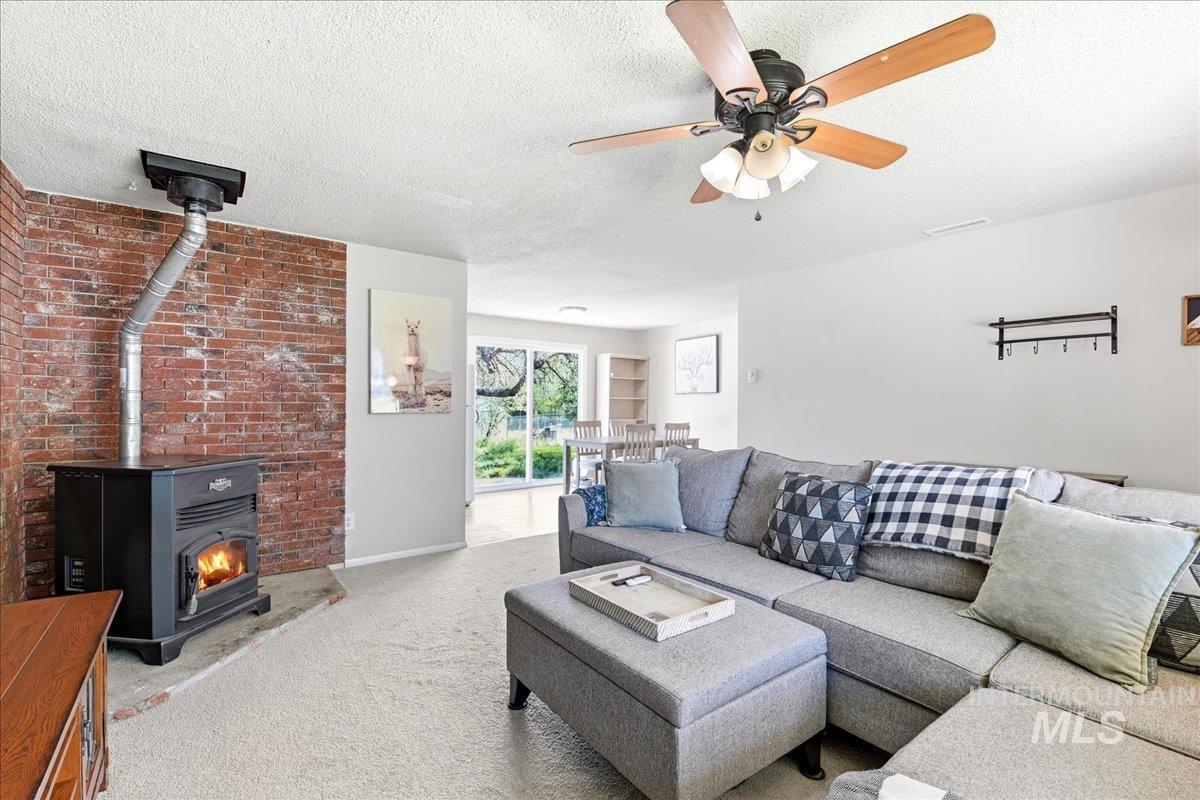 Living area featuring a freestanding wood stove with a brick accent wall, light-colored carpeting, a ceiling fan with integrated lighting, and white walls