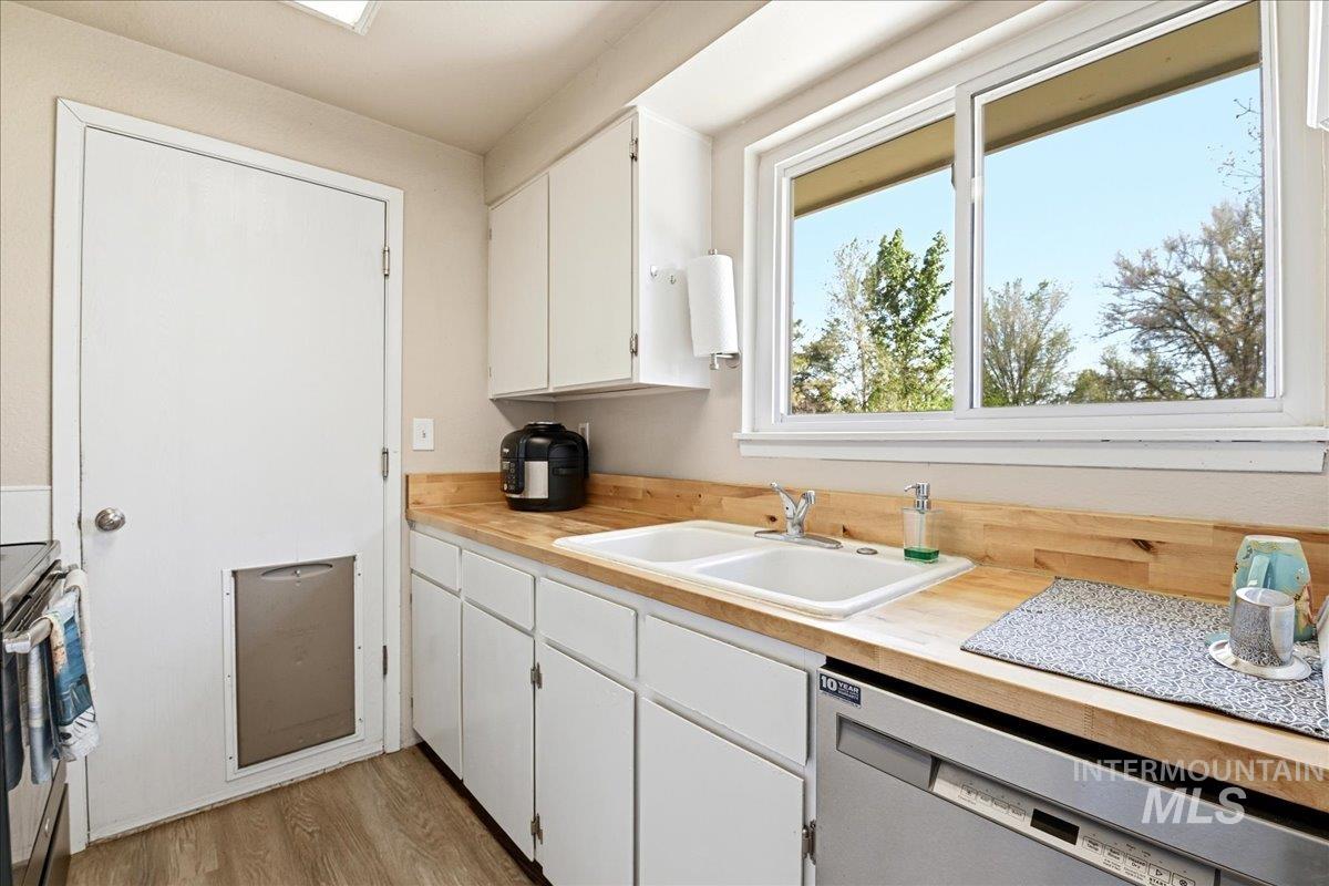 Kitchen featuring a double basin sink, wood-finish countertops, white cabinetry, and stainless steel dishwasher