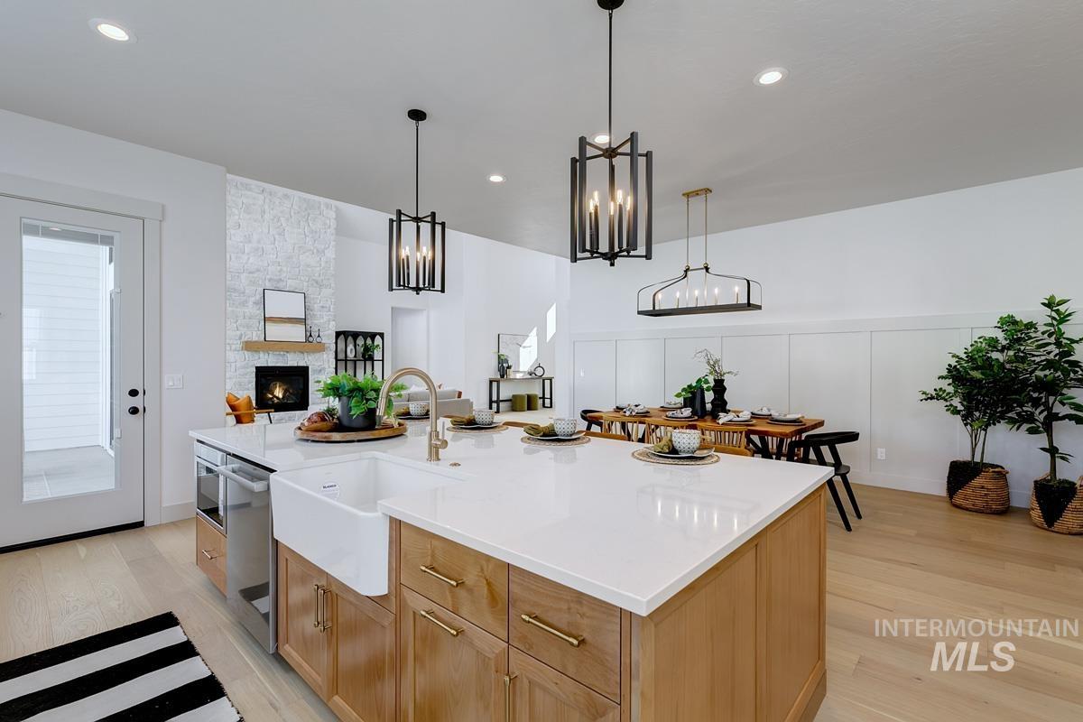 Kitchen featuring light wood finished floors, an island with sink, decorative light fixtures, light stone counters, and stainless steel dishwasher