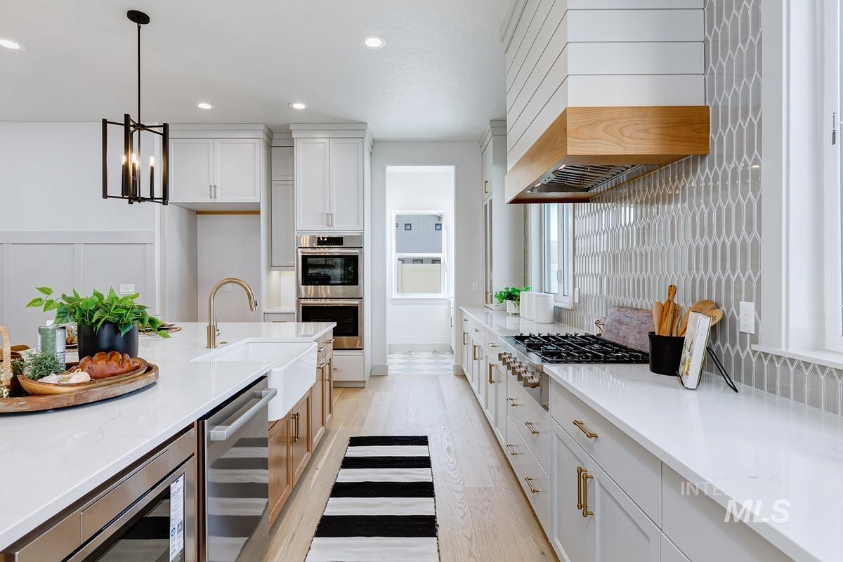 Kitchen with light wood-style floors, white cabinetry, hanging light fixtures, light stone countertops, and appliances with stainless steel finishes
