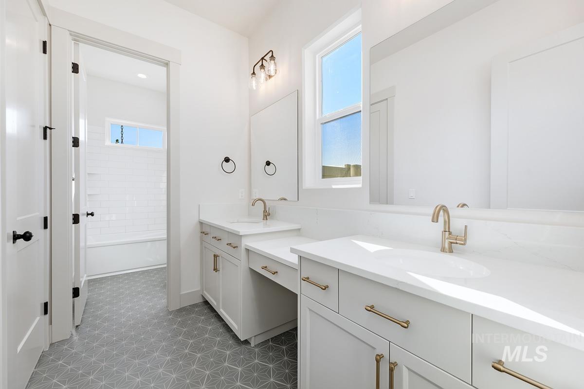Full bath with healthy amount of natural light, two vanities, shower / bath combination, and light tile patterned floors