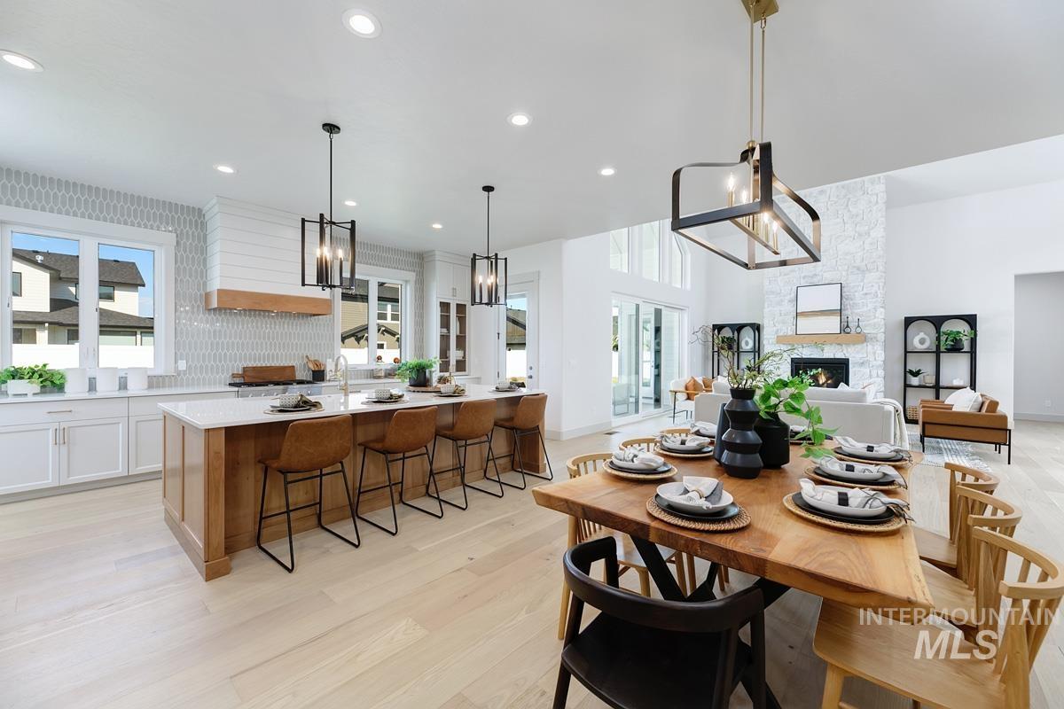 Dining area with light wood finished floors, a stone fireplace, and recessed lighting