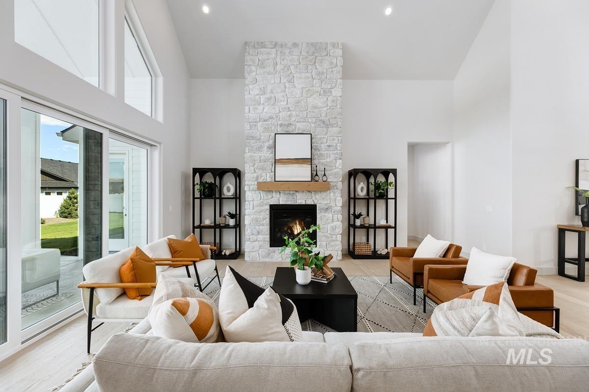 Living room with high vaulted ceiling, a stone fireplace, light wood-style floors, and recessed lighting