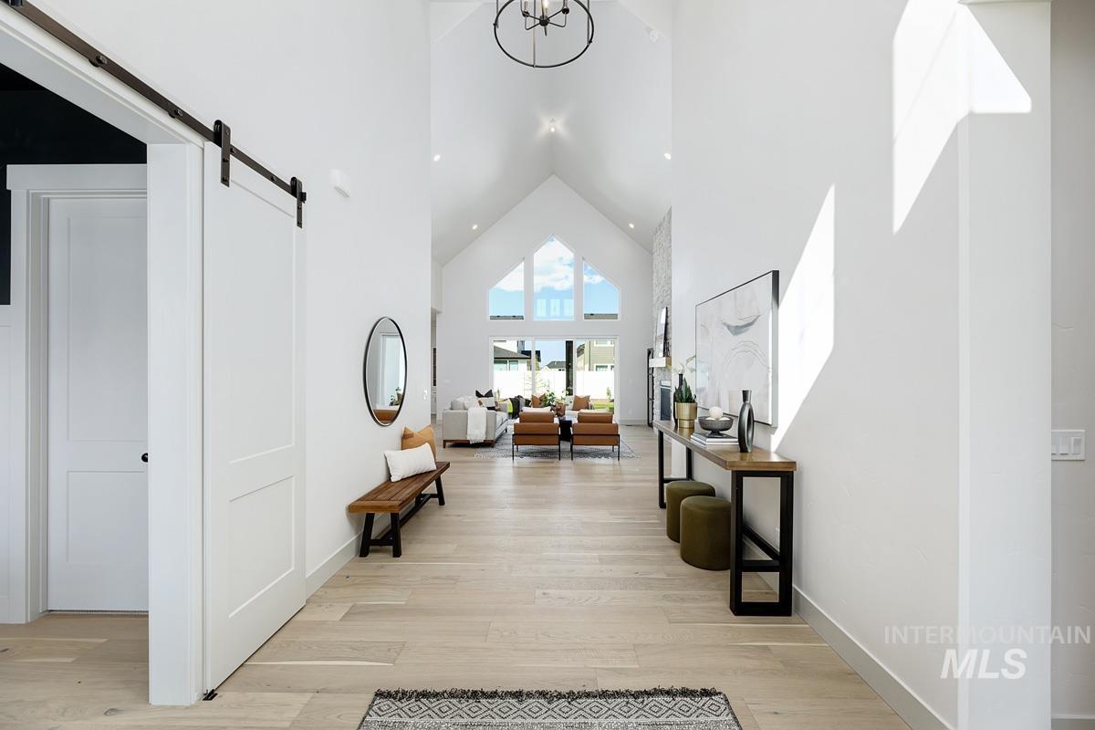 Corridor with high vaulted ceiling, a barn door, light wood-type flooring, and a chandelier