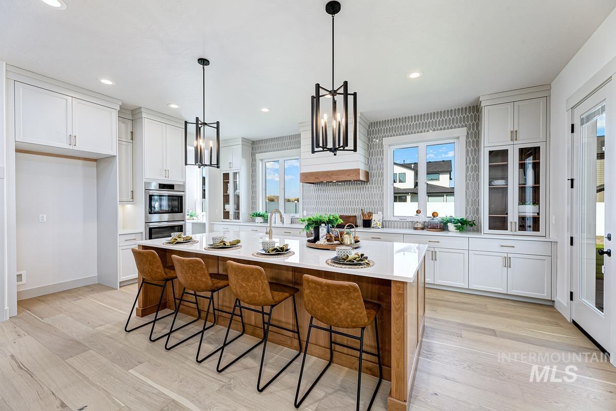 Kitchen with a breakfast bar area, white cabinets, light wood-style floors, a center island with sink, and decorative light fixtures