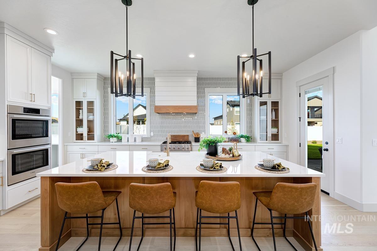 Kitchen with glass insert cabinets, a chandelier, a kitchen island with sink, and recessed lighting