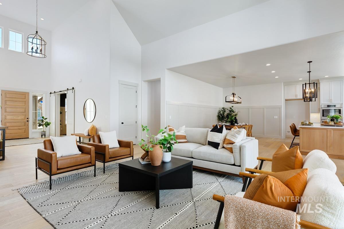 Living area with light wood-style floors, a chandelier, recessed lighting, a barn door, and a towering ceiling
