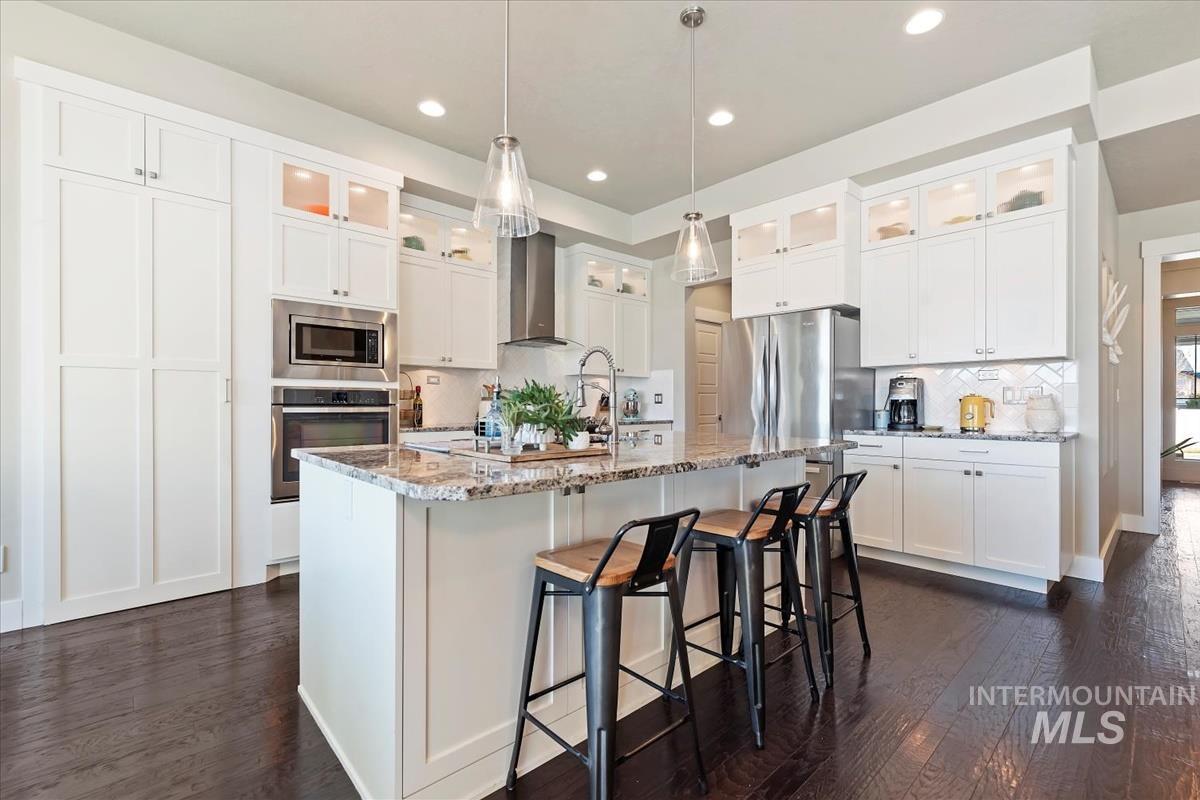 Kitchen featuring light stone countertops, appliances with stainless steel finishes, a kitchen breakfast bar, decorative light fixtures, and wall chimney range hood