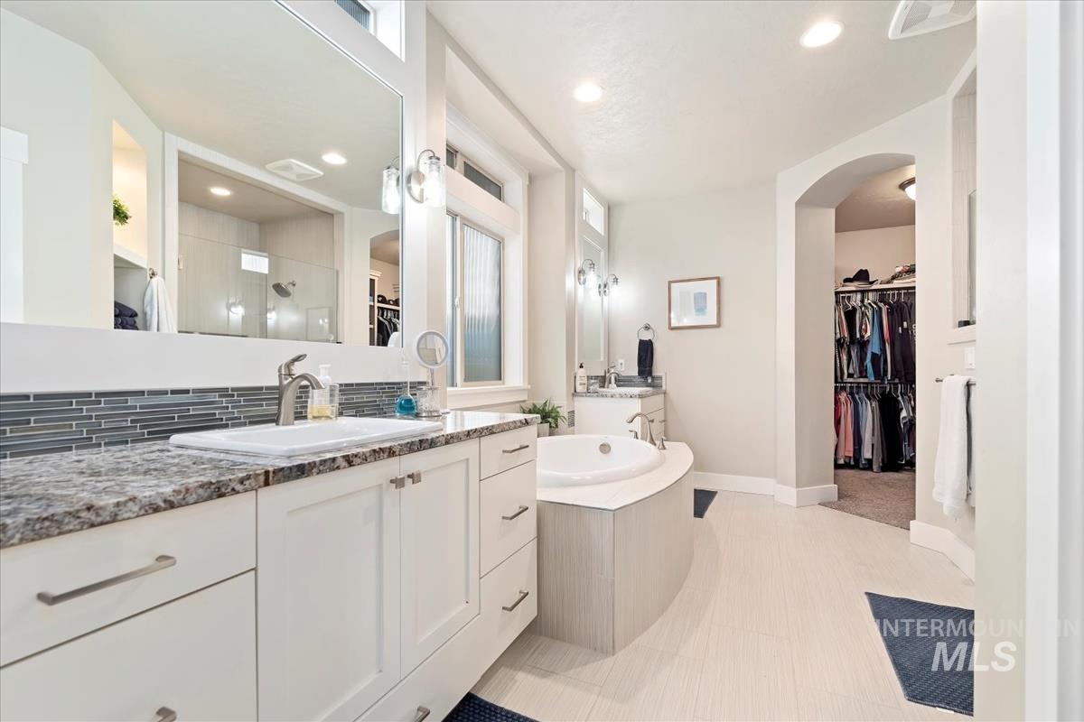 Bathroom featuring a spacious closet, vanity, a bath, tasteful backsplash, and a shower stall