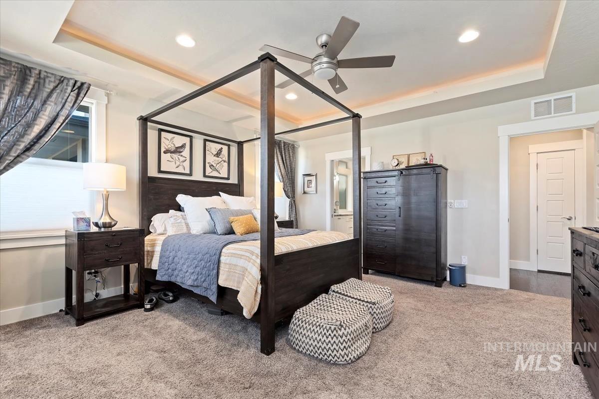 Bedroom with a tray ceiling, light colored carpet, ceiling fan, ensuite bathroom, and recessed lighting
