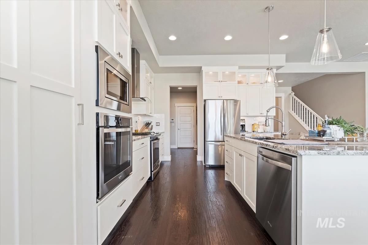 Kitchen with glass insert cabinets, stainless steel appliances, white cabinetry, pendant lighting, and light stone countertops