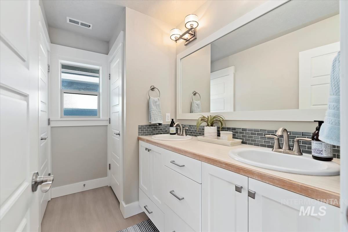 Bathroom featuring double vanity, backsplash, and light wood-style floors