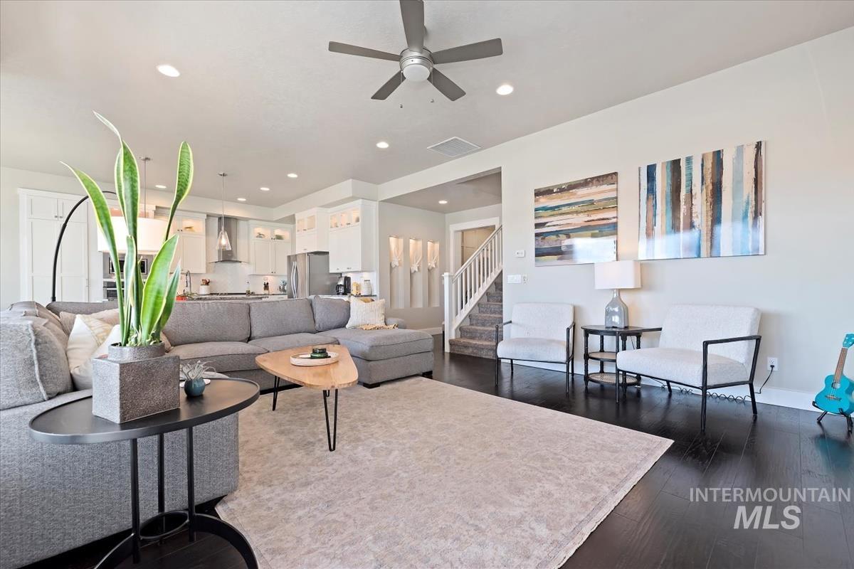 Living room with dark wood finished floors, ceiling fan, recessed lighting, and stairway