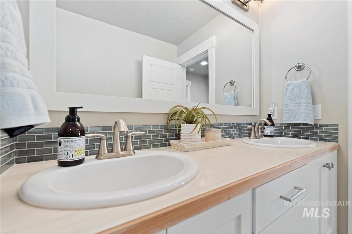 Full bathroom featuring double vanity and decorative backsplash