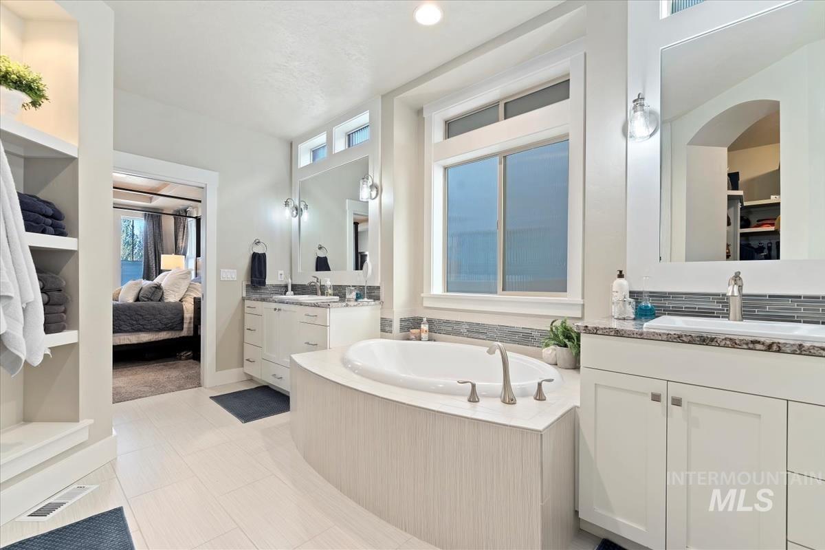 Bathroom featuring two vanities, plenty of natural light, a bath, and ensuite bath